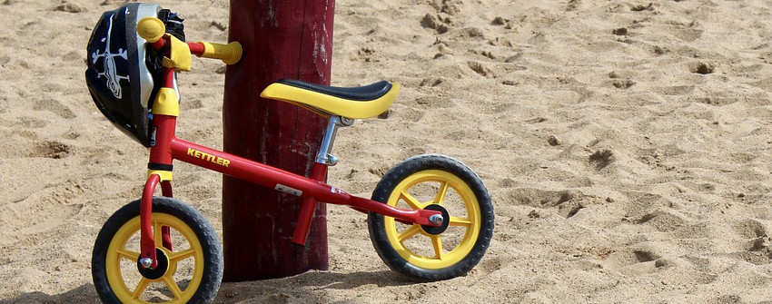 Ett barn som ställt sin cykel lutad mot en stolpe på stranden och hängt sin cykelhjälm på styret.
