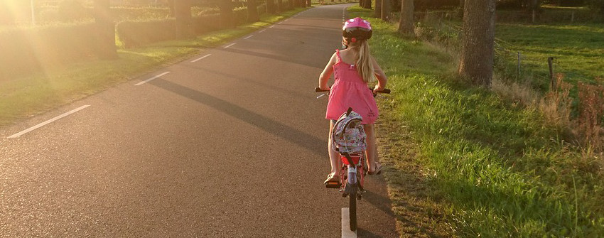 Flicka i rosa klänning som cyklar längs en landsväg